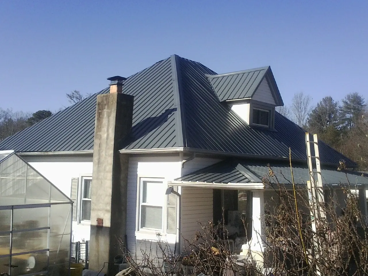 Dark blue standing seam metal roof on a white farmhouse with dormer — Slate & Tile Roof Repair by Roofing Brothers in Buford