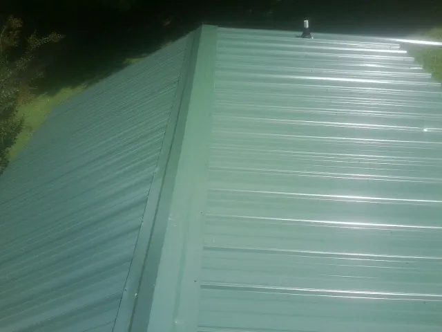 New green metal panels meeting at the ridge of a roof — Flat Roof Repair work by our crew in Buford