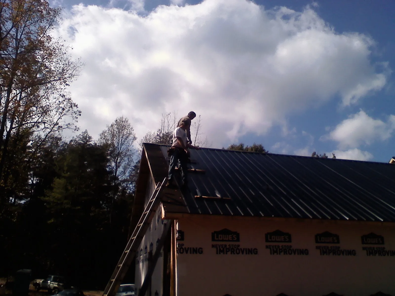 Roofer fastening dark metal panels high against a cloudy sky, from a Roof Inspection job in Buford