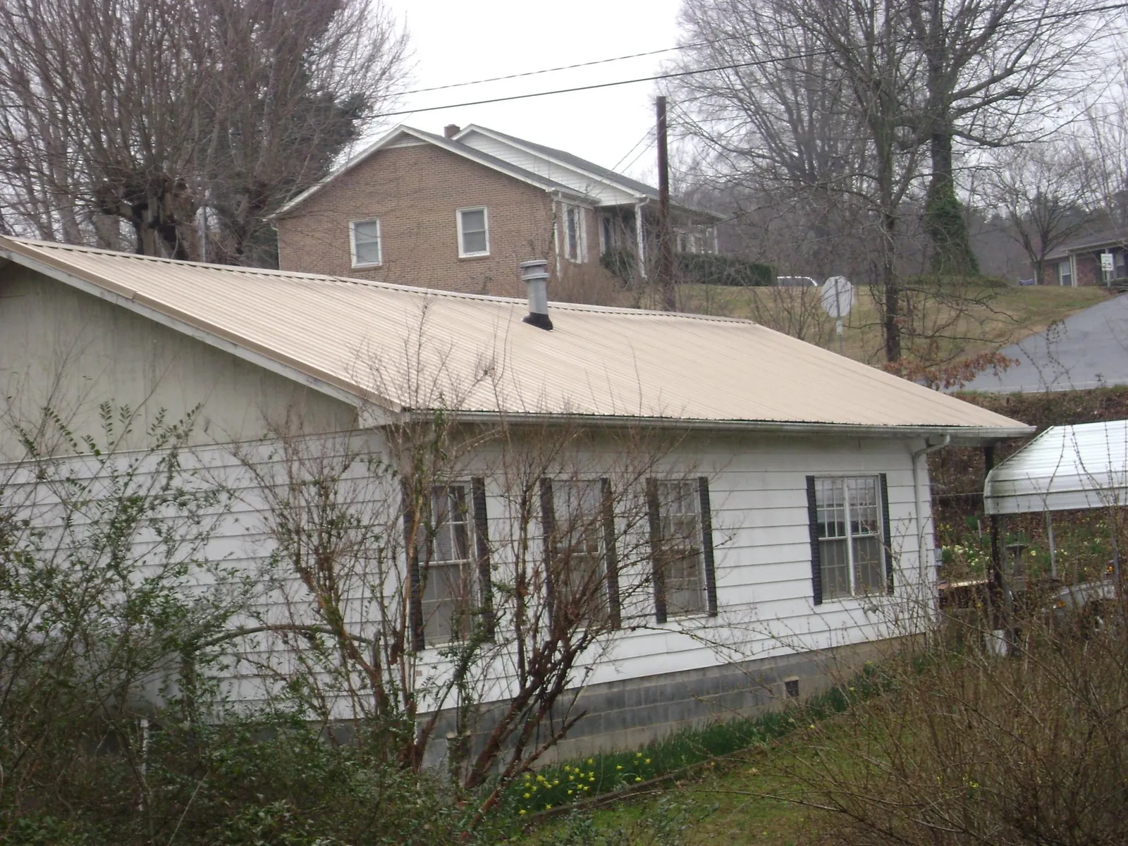 Tan metal roof on a white sided house set into a hillside — Commercial Roofing by Roofing Brothers in Buford